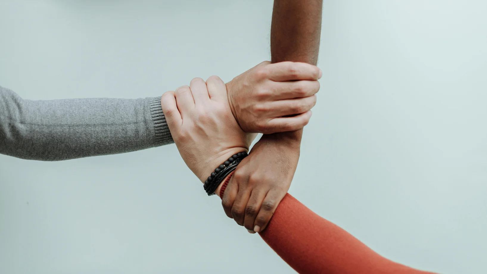 Three individuals' hands connected in a symbol of teamwork and diversity.