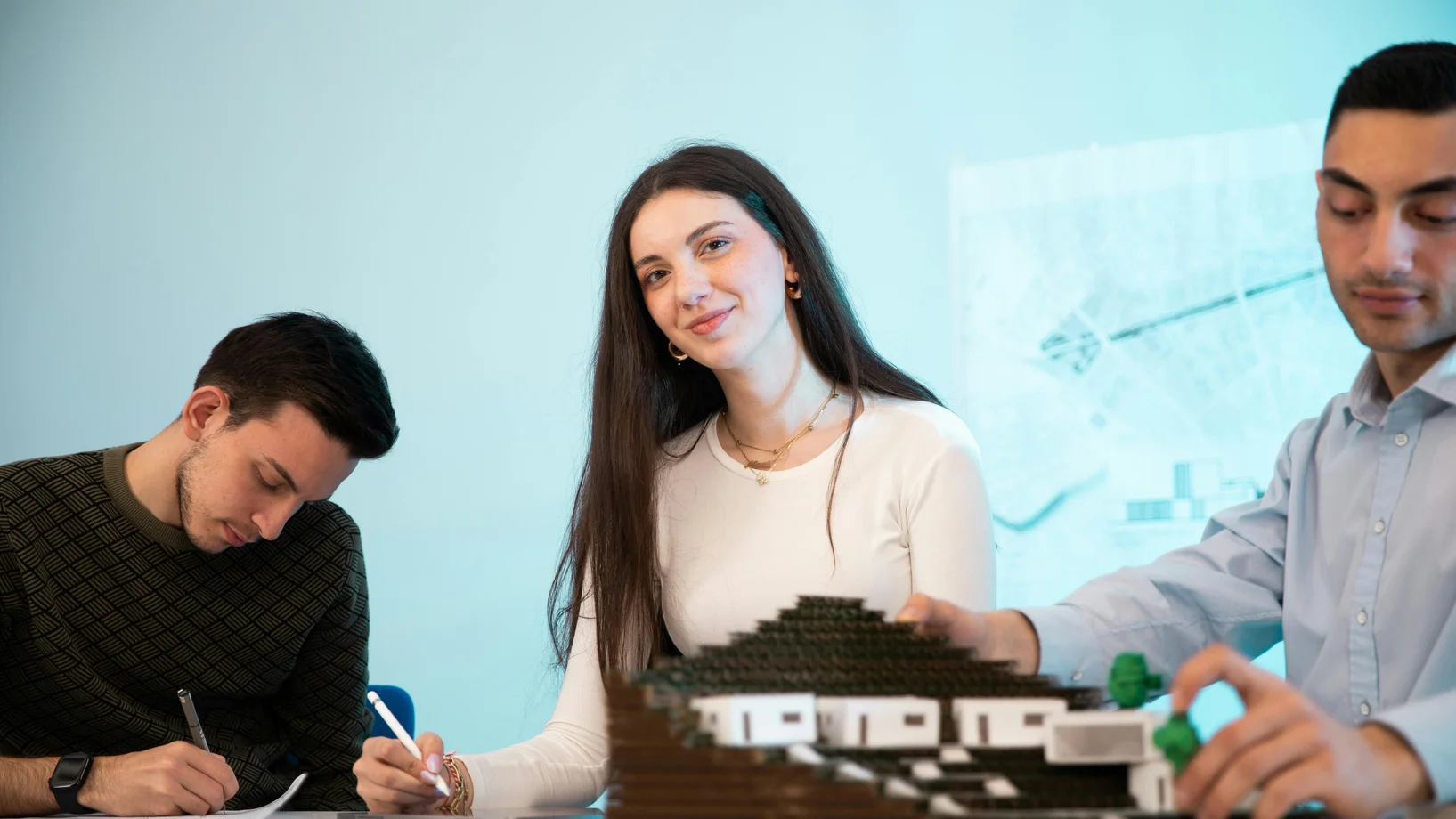 Three people collaborating on an architectural model in an office setting, emphasizing teamwork.